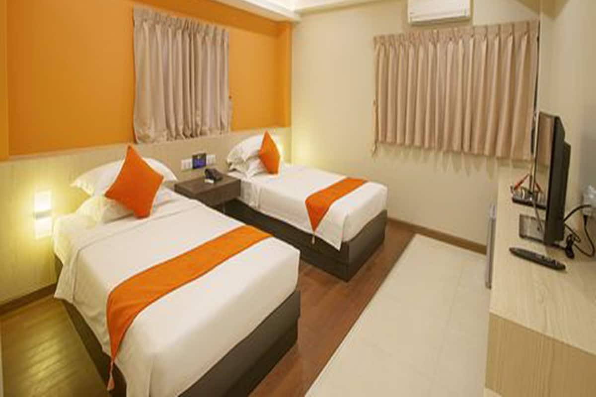 A hotel room with two beds, a desk, a TV, and an air conditioning unit.
