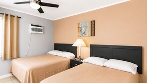 Ein Hotelzimmer mit zwei Betten, einem Deckenventilator, einer Klimaanlage, einer Nachttischlampe und einem Bild an der Wand.