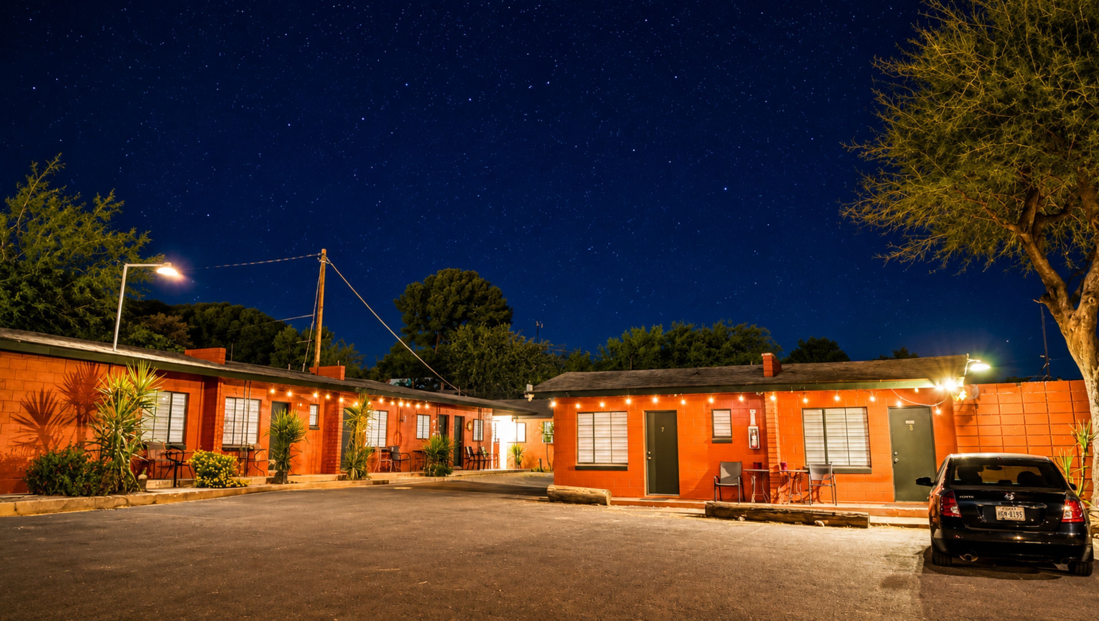 Un motel con varias habitaciones, un estacionamiento y un coche aparcado delante.