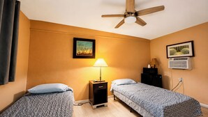A room with two single beds, a ceiling fan, a nightstand with a lamp, an air conditioner, and two framed pictures on the wall. - Copper Mountain Motel (Superior)