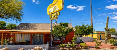 Un motel con letrero amarillo, asientos al aire libre y un cactus en primer plano.