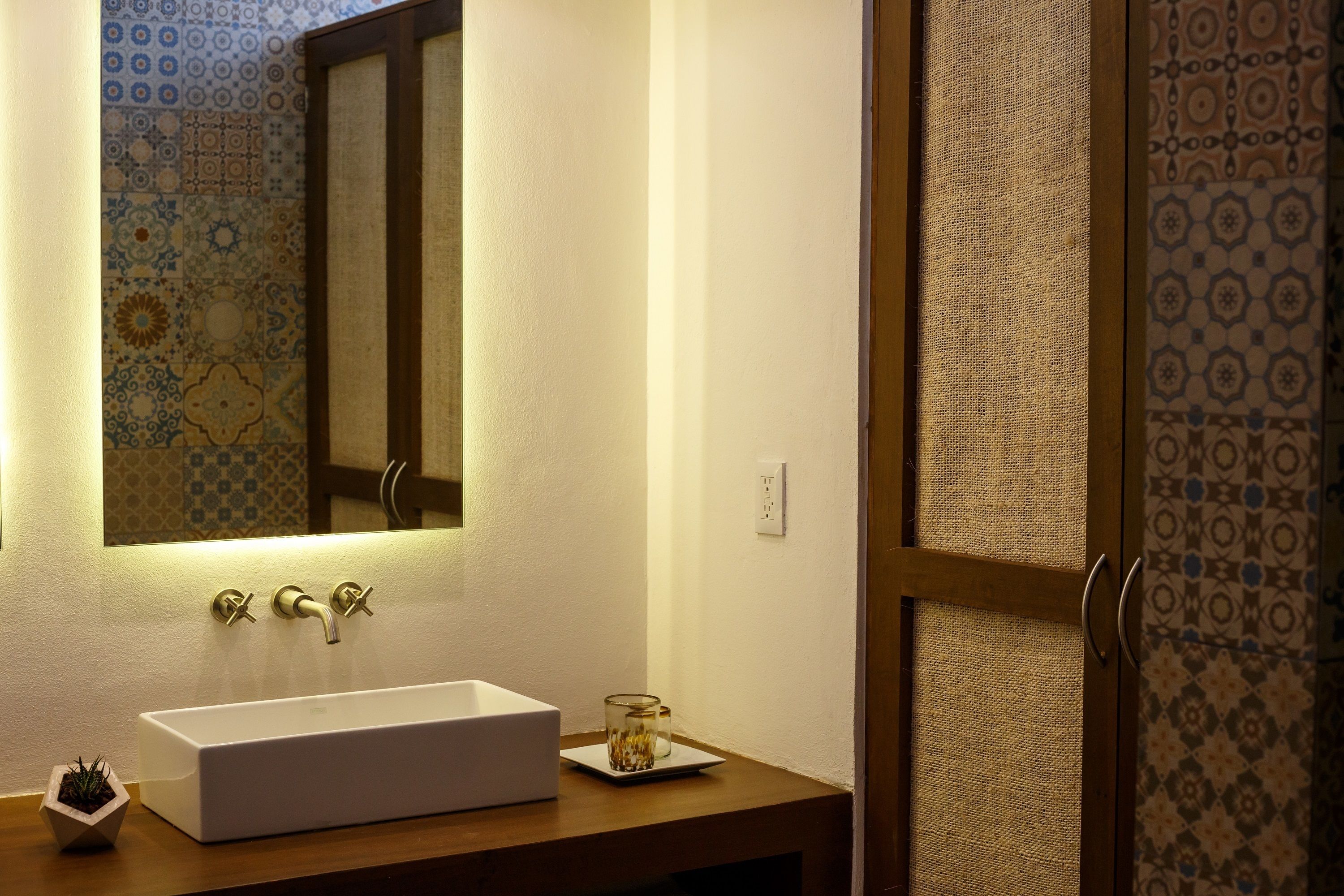 A bathroom with a white sink, a mirror, and patterned tiles on the walls.
