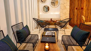 Ein stilvoller Lounge-Bereich mit schwarzen Metallstühlen, einem Holztisch und einer Bank. An der Wand befinden sich drei runde Spiegel, und zur Rechten ist ein Wandpaneel mit Struktur zu sehen.
