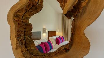 A room with a unique wooden frame mirror reflecting a bed with white and colorful pillows.