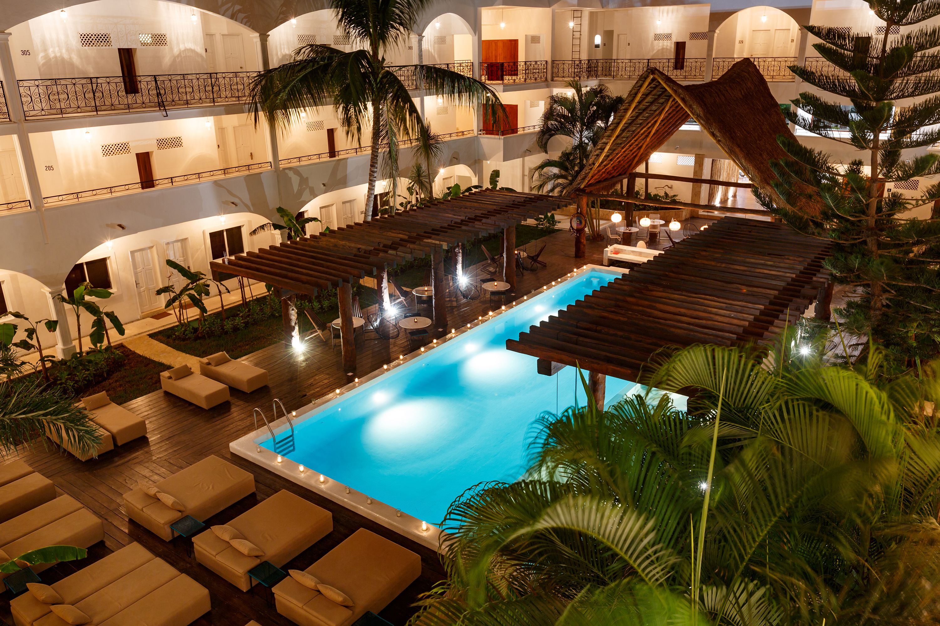 A multi-level hotel with a central swimming pool, outdoor seating, and palm trees.