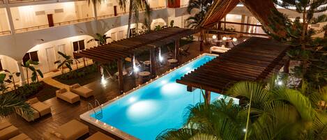 A multi-level hotel with a central swimming pool, outdoor seating, and palm trees.
