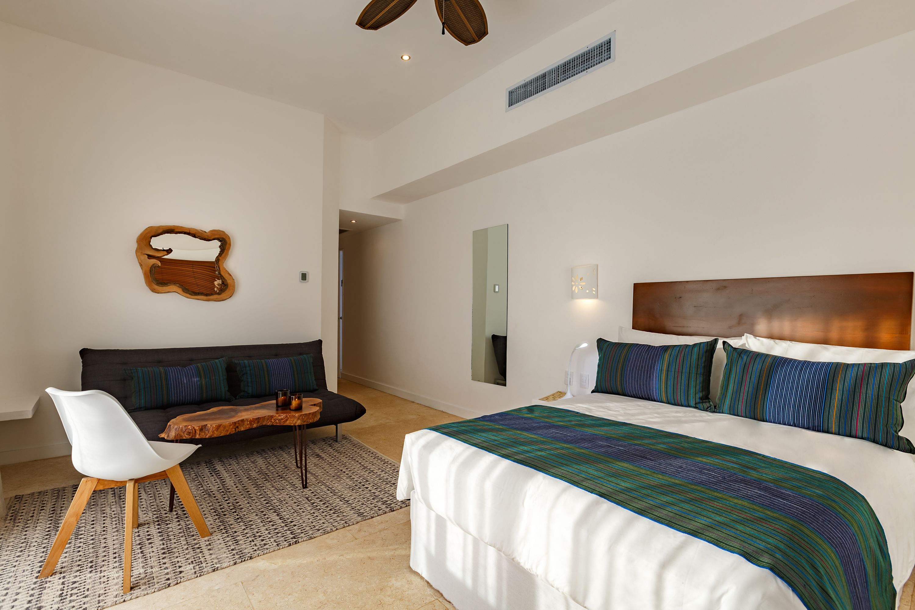 Una habitación de hotel moderna con una cama grande, un sofá, una mesa de centro de madera y una silla blanca.