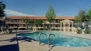 Una piscina con borde de baldosas, rodeada por una valla, y un edificio al fondo.