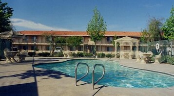 Una piscina con borde de baldosas, rodeada por una valla, y un edificio al fondo.