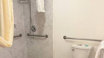 A bathroom with a shower, toilet, and a trash bin.