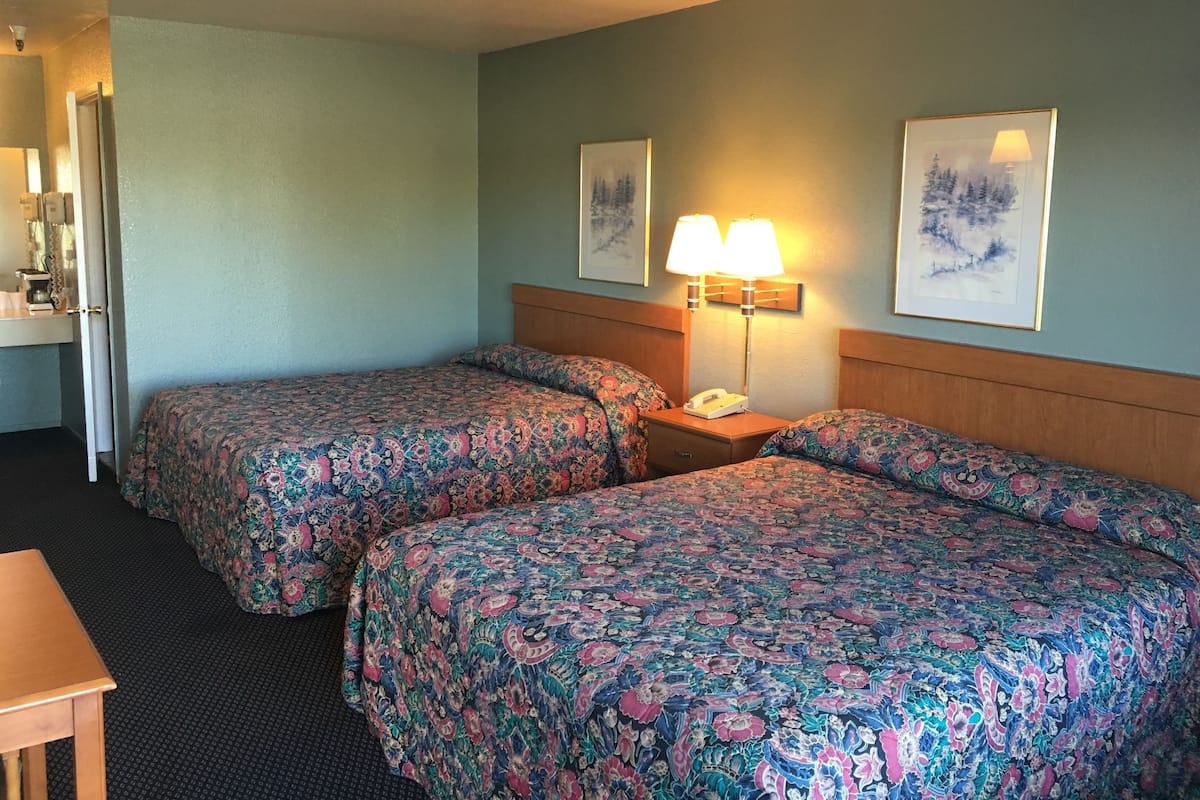 A hotel room with two beds, a desk, a lamp, and a phone on the nightstand.