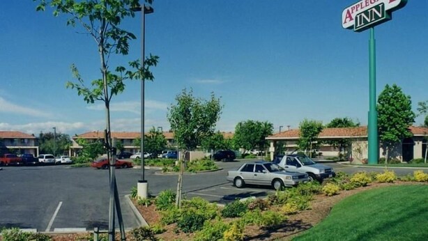 Un estacionamiento con varios coches, un cartel de Apple Inn y un edificio con techo rojo al fondo.