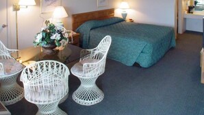 Habitación de hotel con cama, dos sillas blancas, una mesa con un jarrón de flores, dos lámparas de pared y un escritorio con silla.