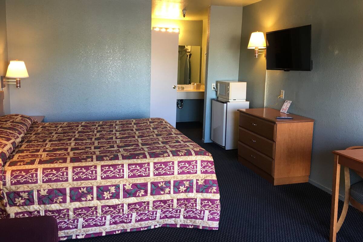 A hotel room with a bed, a dresser, a desk, a television, and a microwave.