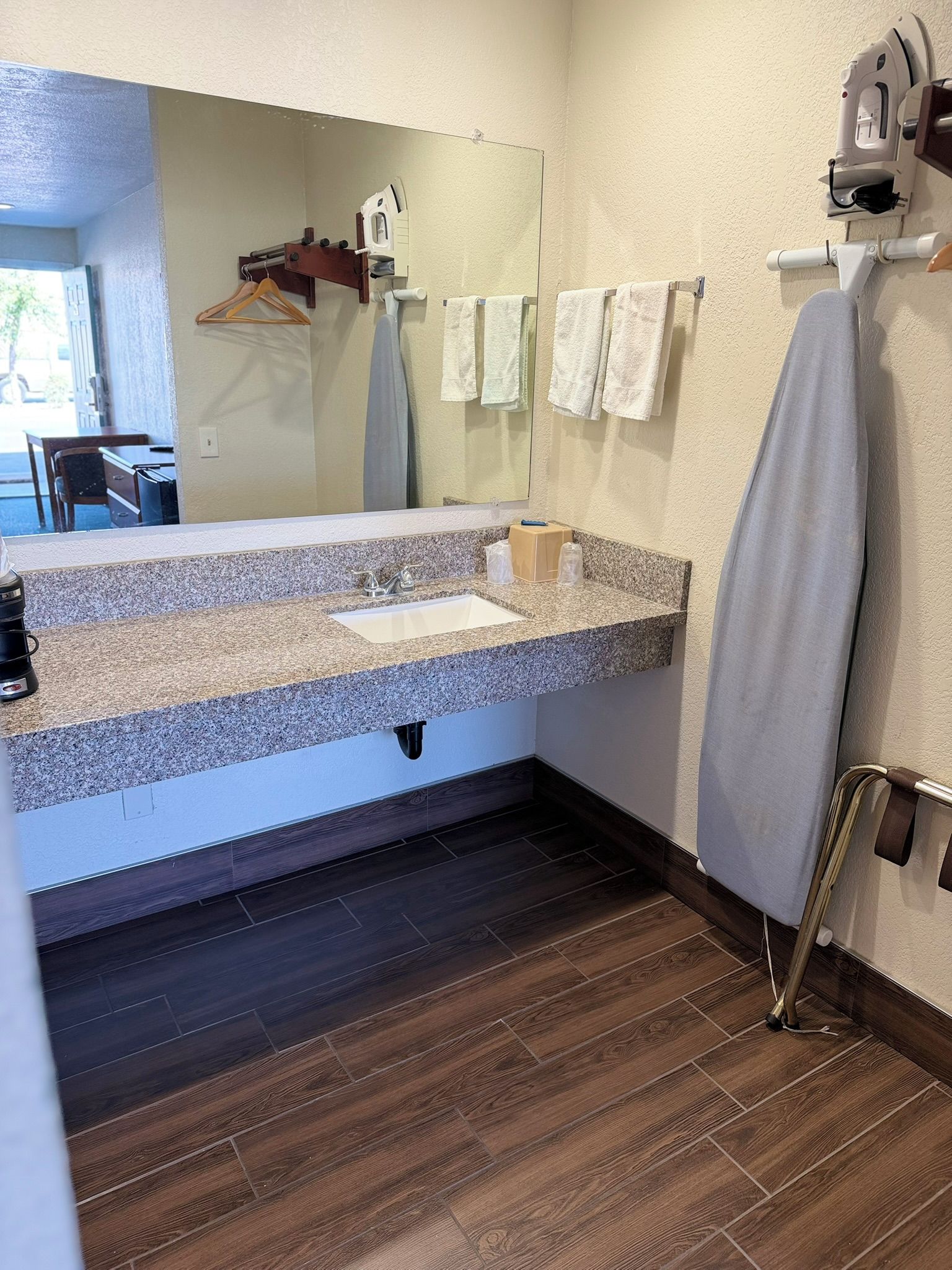 A bathroom with a granite countertop sink, a mirror, a towel rack with towels, and a wooden floor.