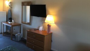 A hotel room with a desk, a dresser, a mirror, a television, and a lamp. - Applegate Inn (Atwater)