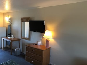 A hotel room with a desk, a dresser, a mirror, a television, and a lamp. - Applegate Inn (Atwater)