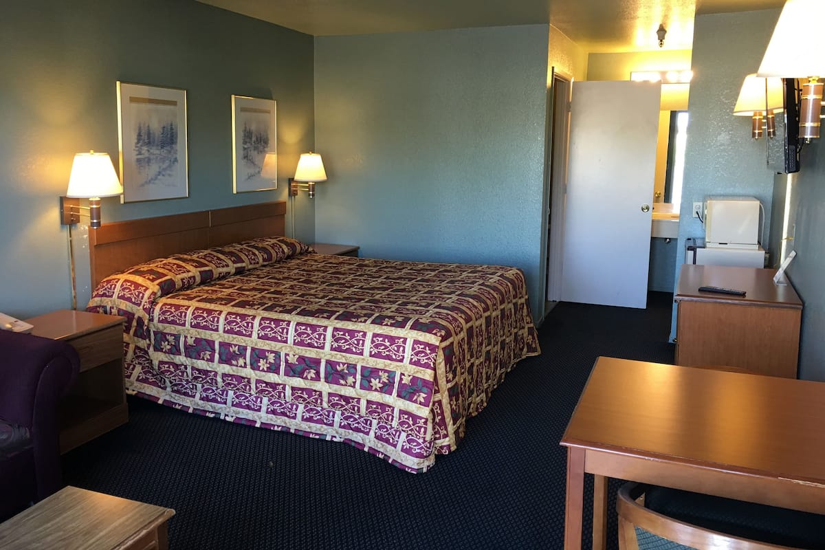 A hotel room with a large bed, two bedside lamps, a desk, and a chair.