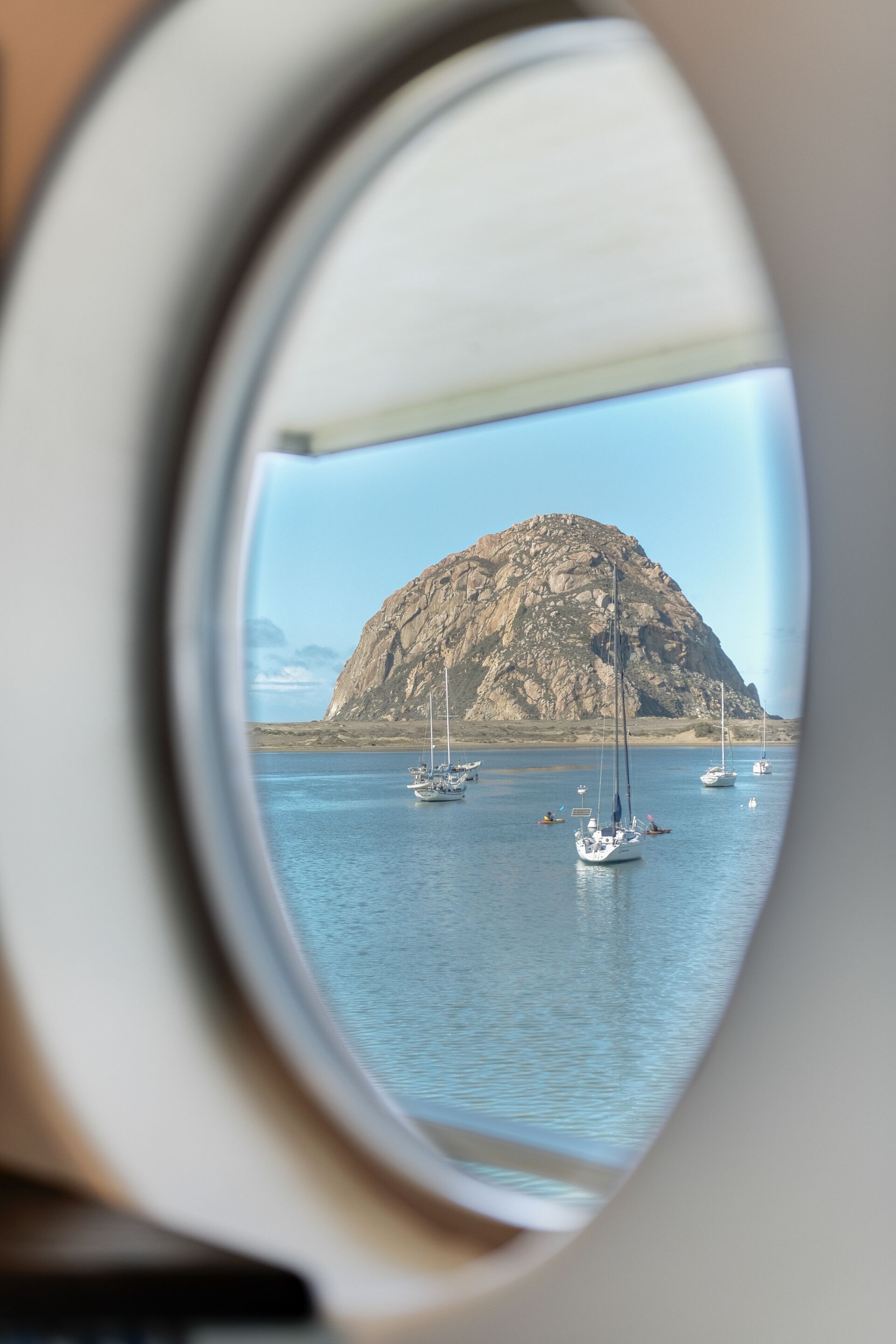 A view through a window of a boat, featuring a rocky island and several sailboats in the water.