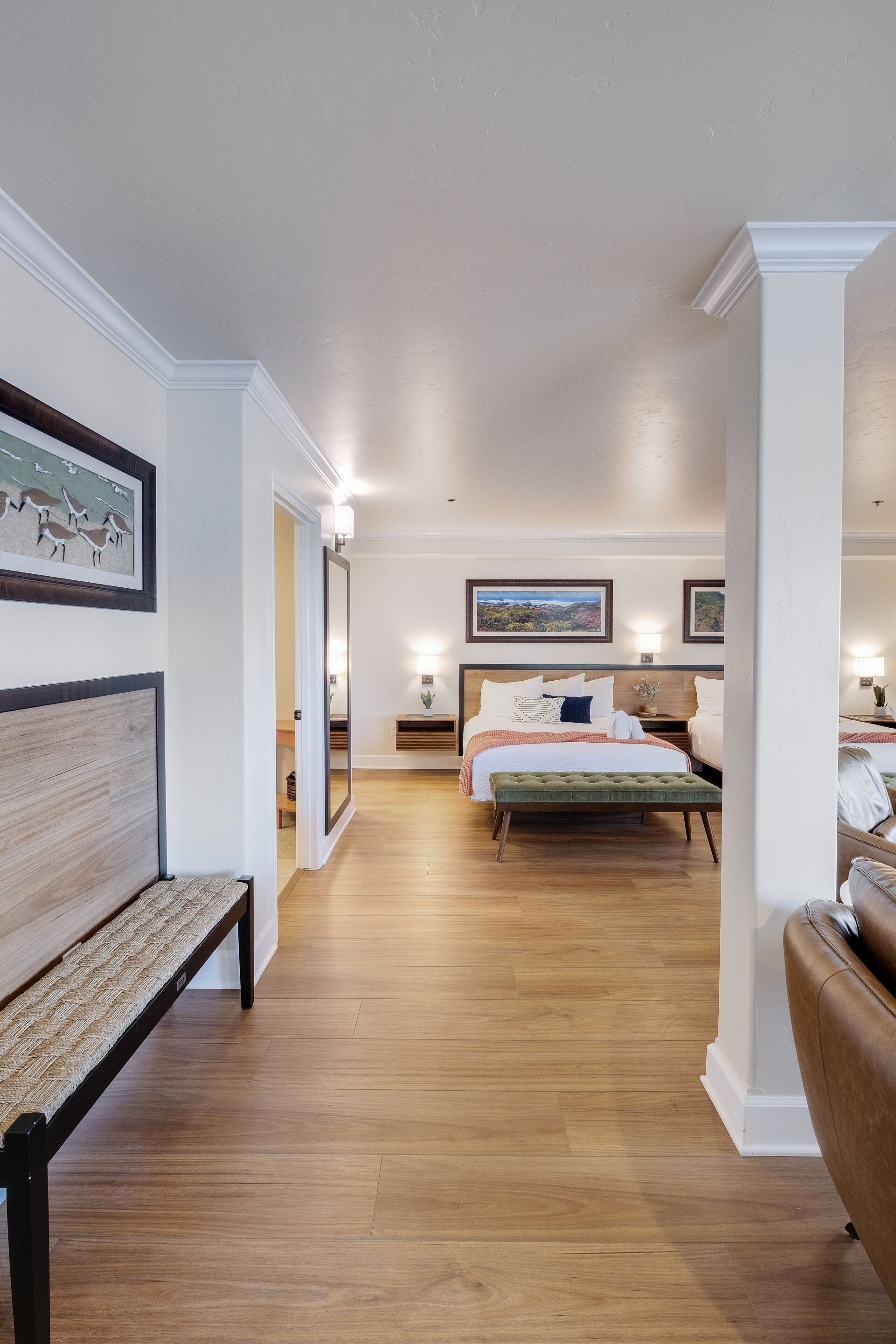 Een hotelkamer met een houten vloer, een bed met een groen gestoffeerde bank, een bruine leren sofa en lijstwerken aan de wanden.