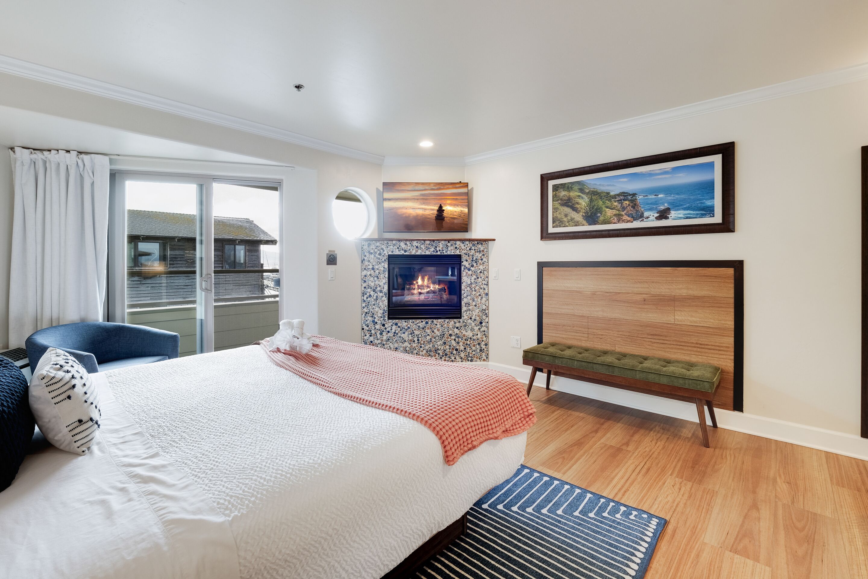 Quarto com cama grande, um banquinho, lareira e vista para o oceano.