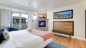 Quarto com cama grande, um banquinho, lareira e vista para o oceano.