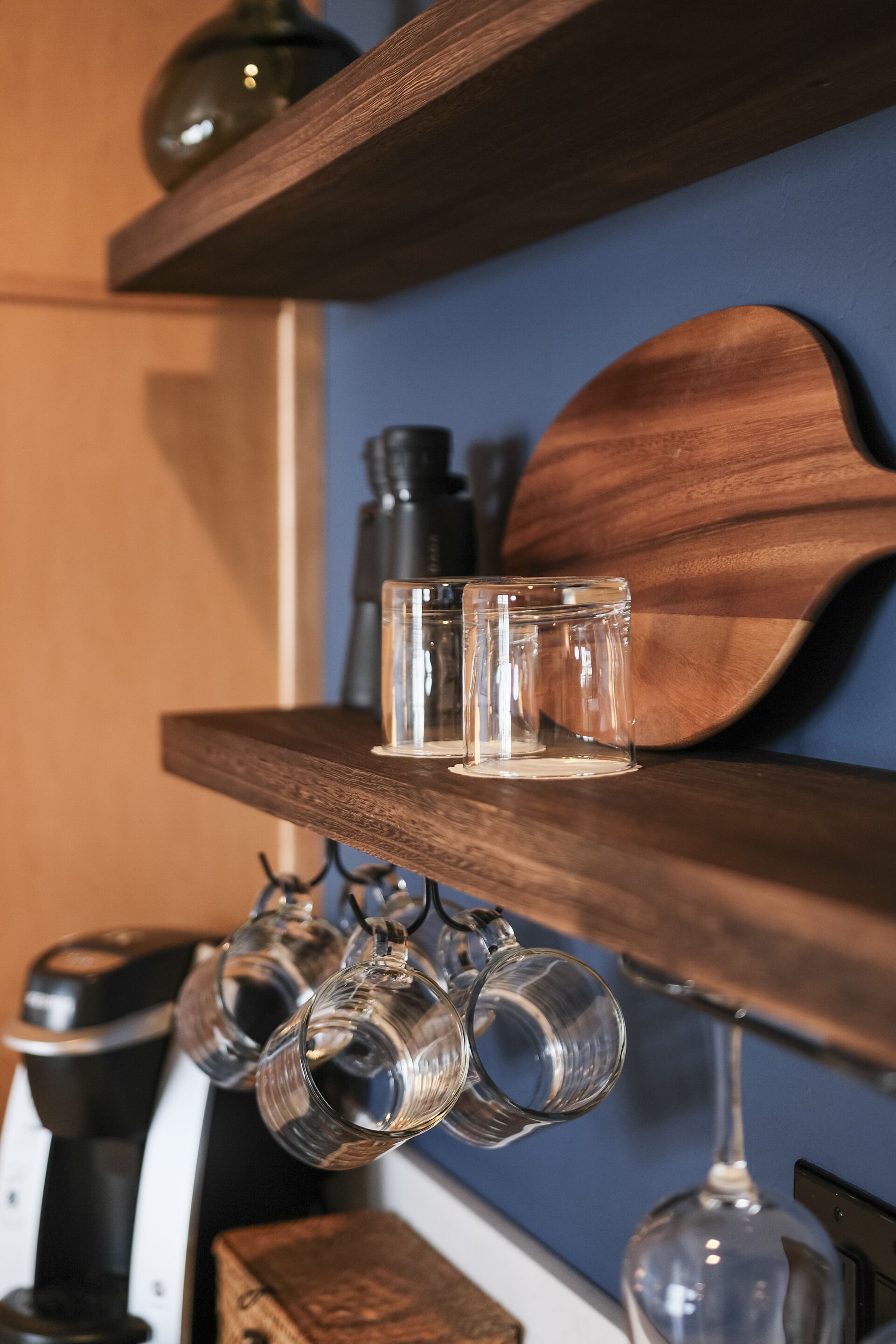 Une étagère en bois avec trois verres transparents et un verre à vin suspendu en dessous.