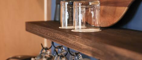 Une étagère en bois avec trois verres transparents et un verre à vin suspendu en dessous.