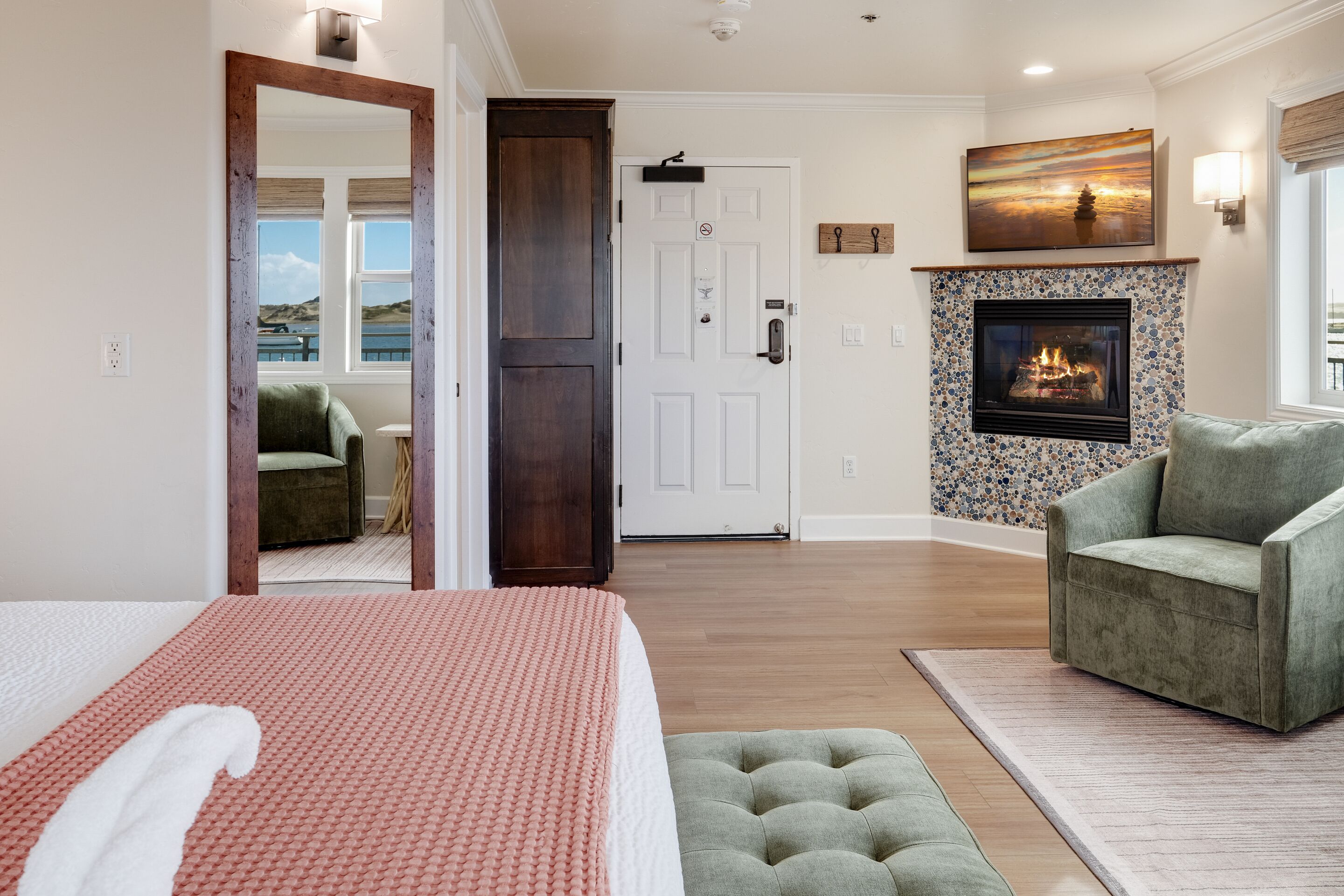 A bedroom with a bed, a green armchair, a fireplace, and a view of the outdoors.
