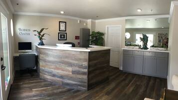 A reception area with a wooden reception desk, a computer, framed certificates on the wall, and a potted plant.