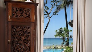 A wooden cabinet with intricate carvings, a view of a pool with a palm tree, and a beach in the background.