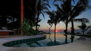 A pool area with lounge chairs and palm trees at sunset.