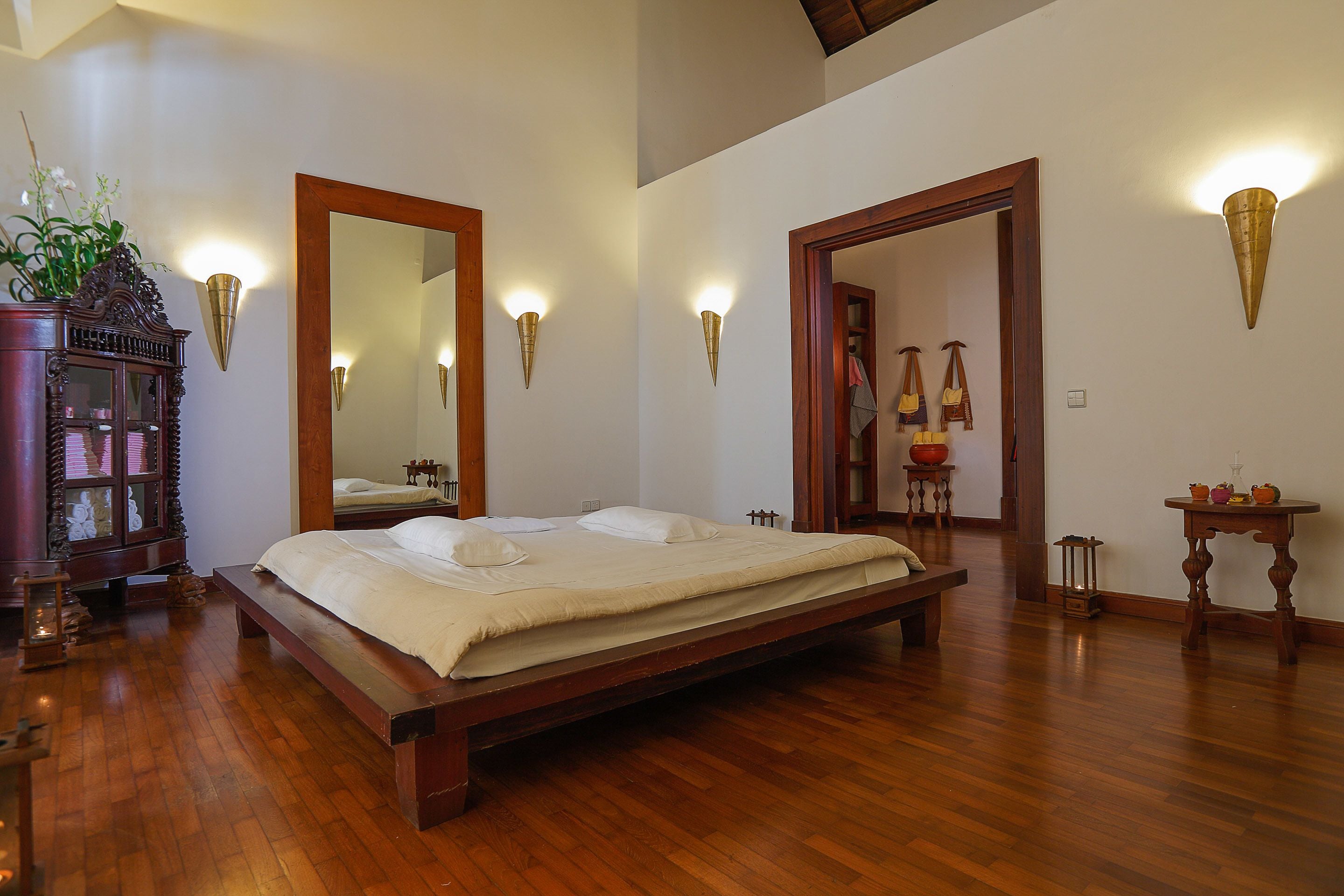 Een ruime slaapkamer met een groot bed, houten vloeren en wandlampen.