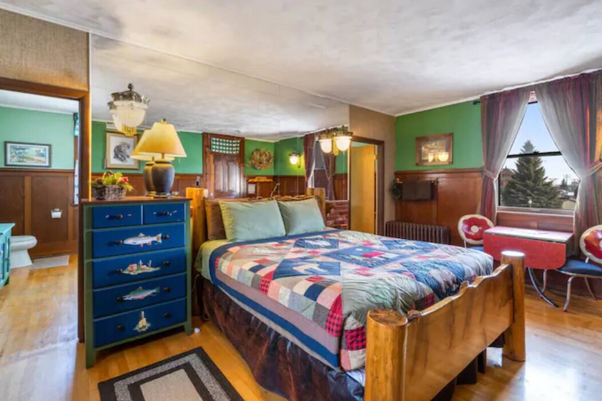 A cozy bedroom with a wooden bed, a dresser with drawers, a desk, and a chair.