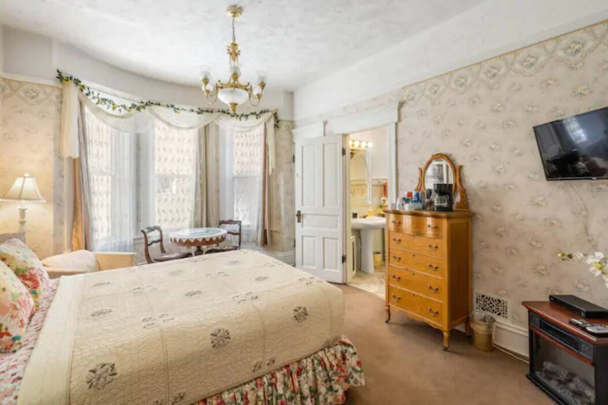 A bedroom with a large bed, a dresser, a vanity, and a television.