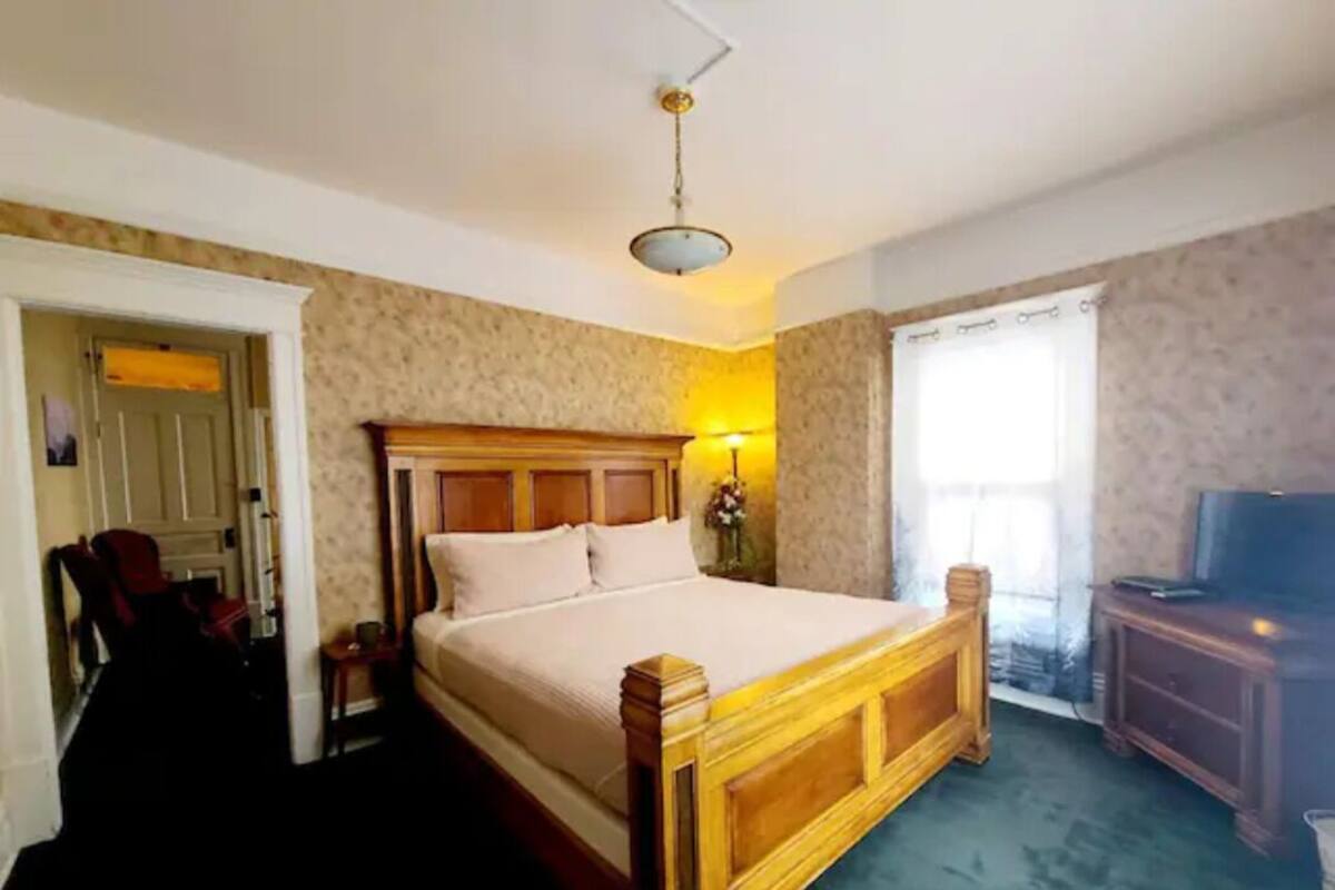 A bedroom with a wooden bed, a television, and a window with curtains.