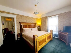 A bedroom with a wooden bed, a television, and a window with curtains.