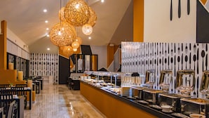 Un espace buffet proposant une variété de plats, un long comptoir avec des ustensiles de service et des lampes suspendues décoratives.