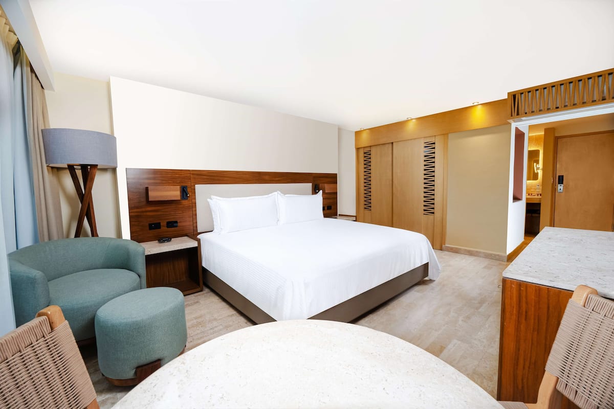 A hotel room with a bed, a desk, a chair, a small table, and a wardrobe.