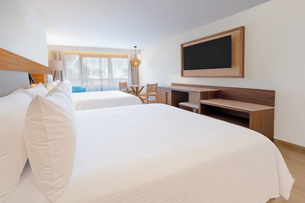 A hotel room with two beds, a desk, a chair, a TV, and a window with curtains.
