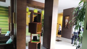 A lobby with a modern design, featuring a seating area with a sofa and chairs, a decorative wooden structure with shelves, and a large potted plant. - Hotel Pho Sein (Yangon)