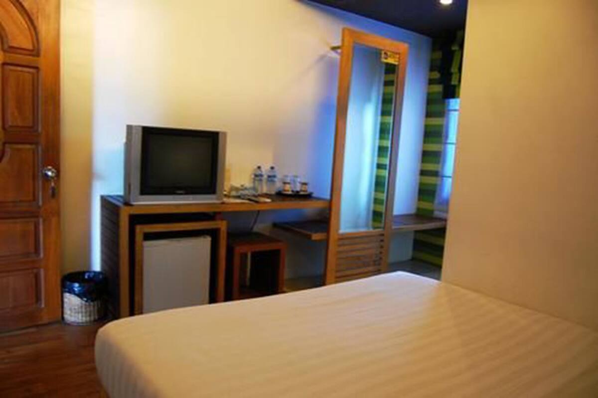 A hotel room with a bed, a desk with a television, and a small table with a trash can.