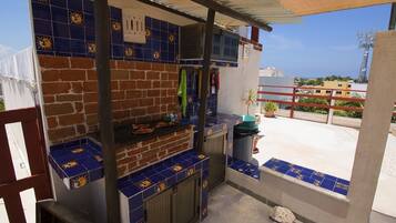 Een buitenkeuken met een bakstenen muur en blauwe tegels, een barbecue en een vuilnisbak.
