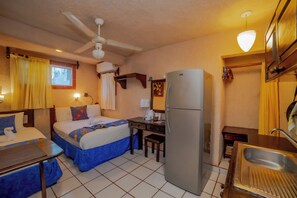 Quarto de hotel compacto com duas camas, uma escrivaninha, um frigorífico e uma pia.