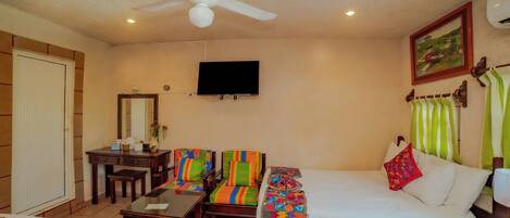 Una habitación de hotel con cama, escritorio, silla, televisor y ventilador de techo.