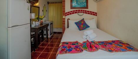 Habitación de hotel con cama, escritorio, refrigerador, aire acondicionado y un cuadro en la pared.
