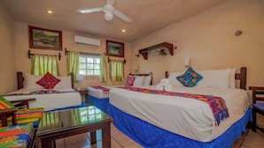 Habitación de hotel con dos camas, ventilador de techo, ventana con cortinas y una mesita.