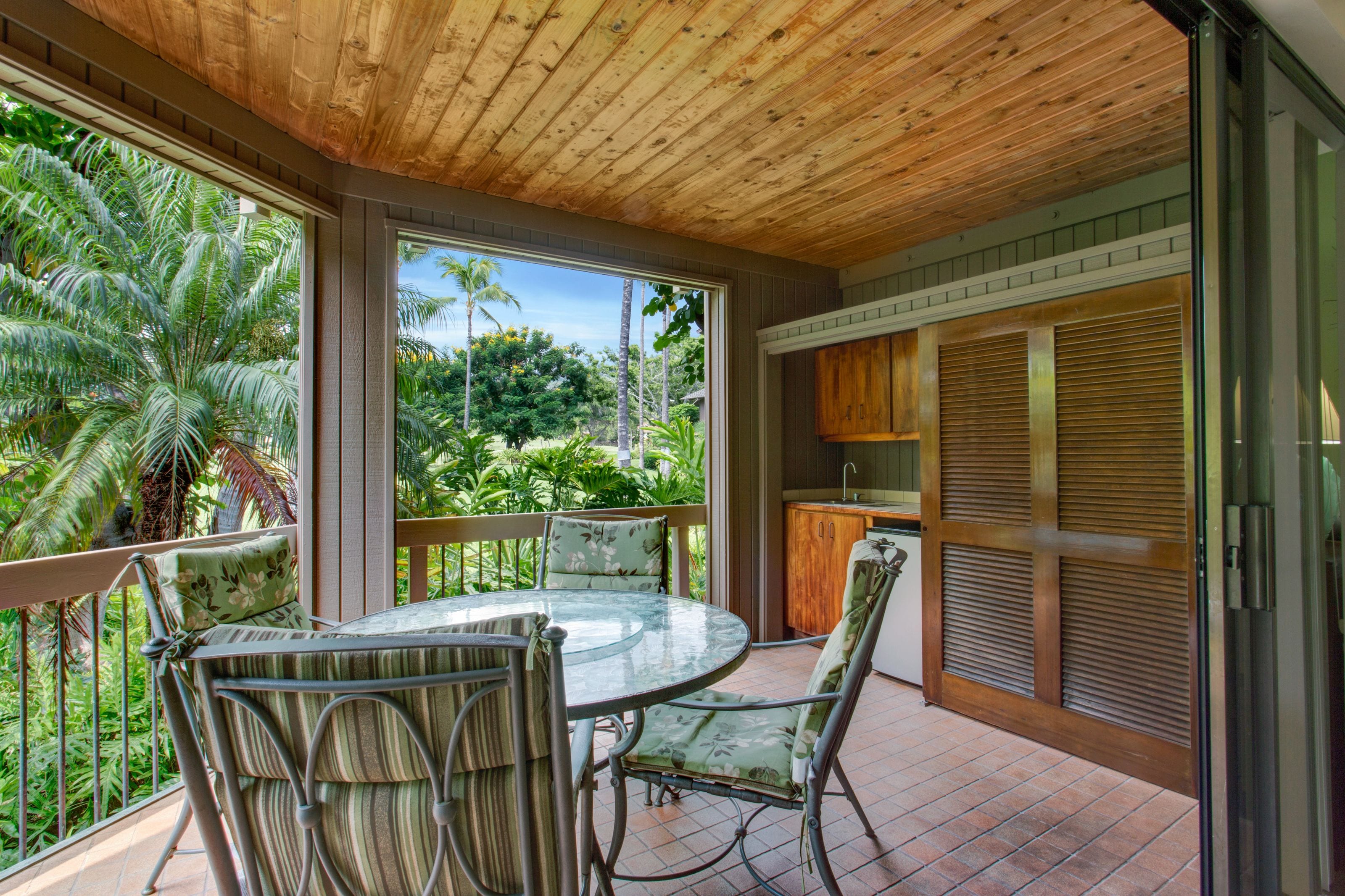 Un patio techado al aire libre con una mesa y sillas de vidrio, techo de madera y vistas a la vegetación tropical.