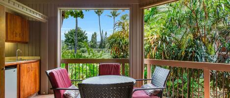 A covered patio with a wooden ceiling, a dining table with chairs, and a view of a lush garden.
