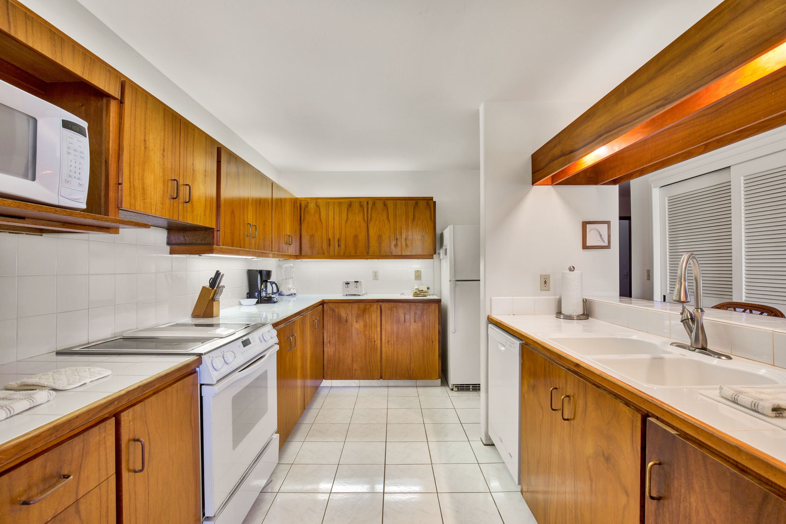 A kitchen with wooden cabinets, a white countertop, a stove, a sink, and a refrigerator.